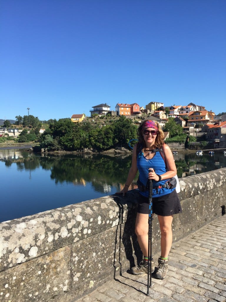 Michelle standing on a Roman Bridge with a hamlet behind her, across the water