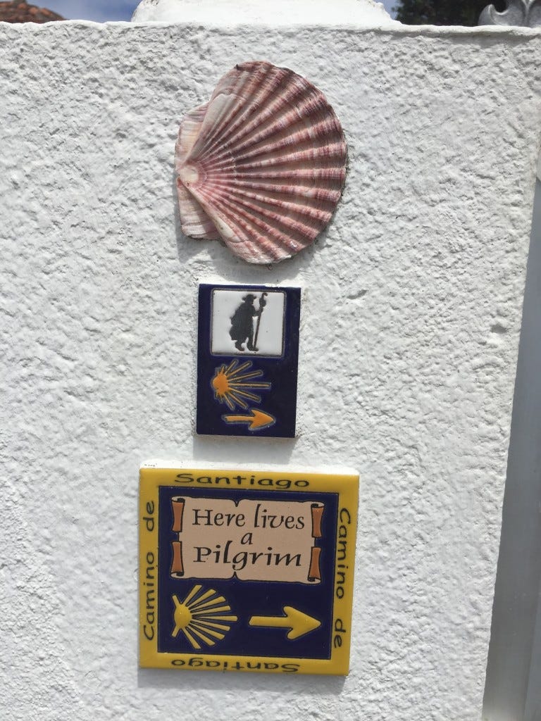 A shell and two ceramic plaques that are mortared to a wall — the plaques have the camino symbol in them.