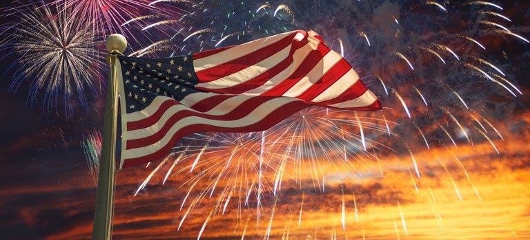 American flag on a pole amid exploding fireworks.
