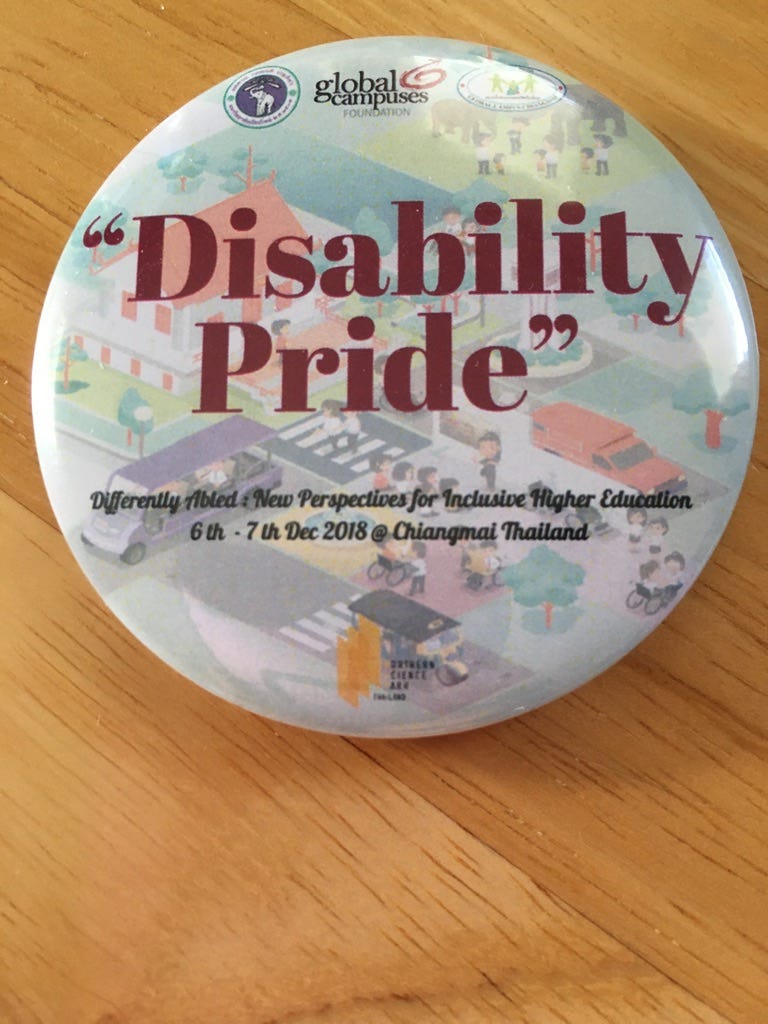 “Disability Pride” button from 2018 conference in Chiang Mai, Thailand, called “Differently Abled: New Perspectives for Inclusive Higher Education,” Dec. 6–7, 2018. Conference information on button below the words, “Disability Pride.” All superimposed on drawing of people with and without wheelchairs by crosswalks and with cars around the people.From the author’s personal collection.