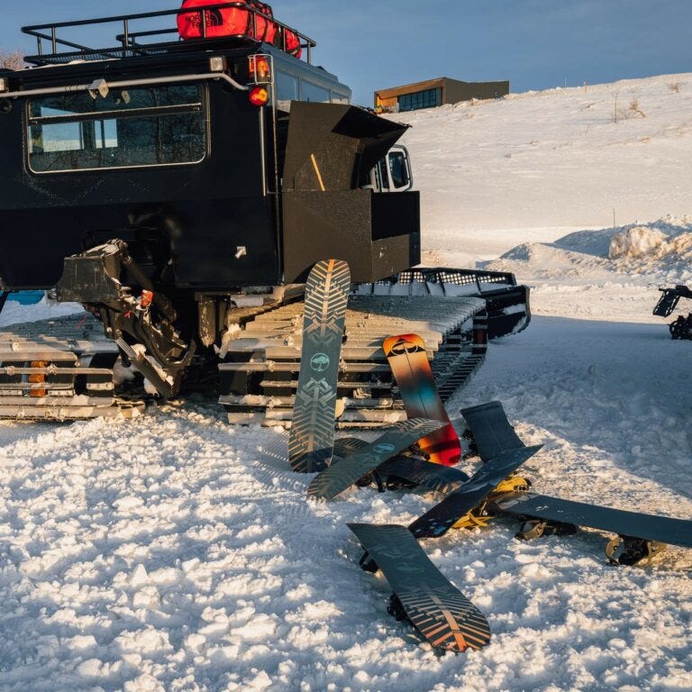 Black camping trailer surrounded by snow with 9 Arbor snowboards placed in front of the trailor.