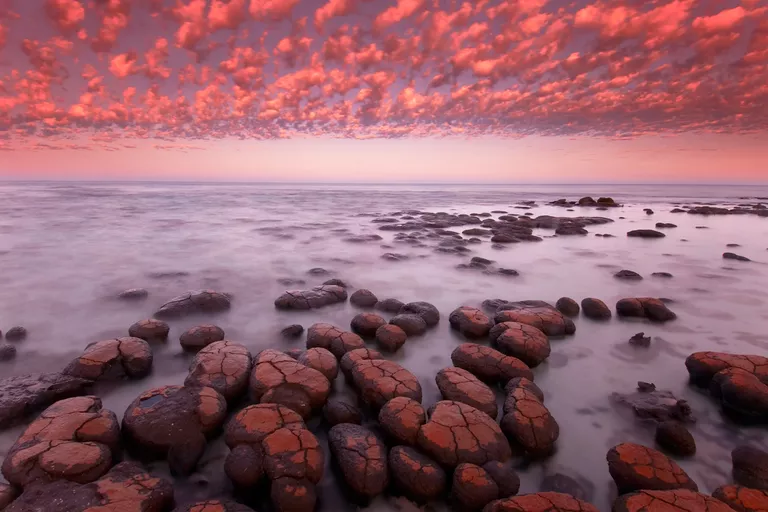 Photograph of Earth landscape looking like another planet — red sky, mist on ocean, rock-like stromatolites and no other life