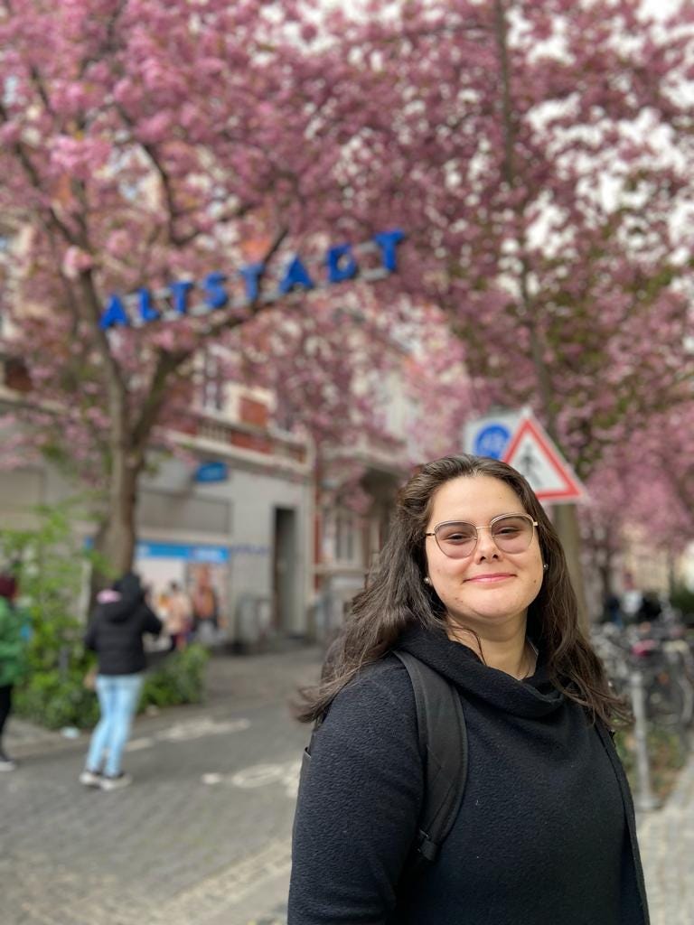 A girl smiles as she poses with a sign that reads Altstadt on the background and the cherry blossoms in the streets of Bonn.