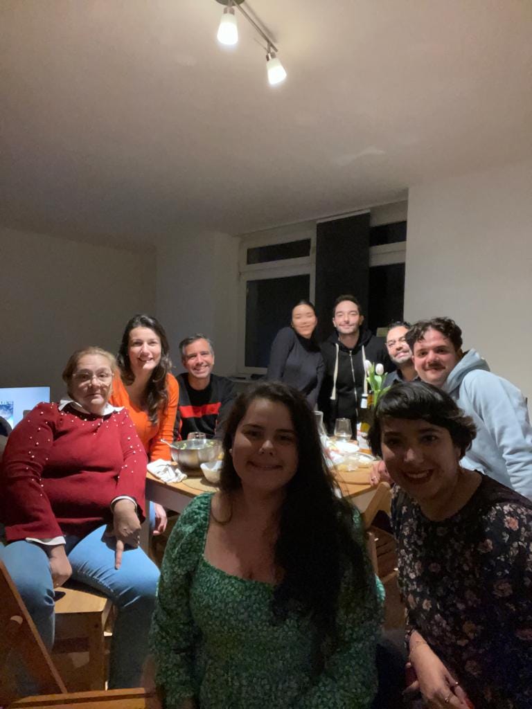 Nine people pose in a house while around a table with food and drinks.
