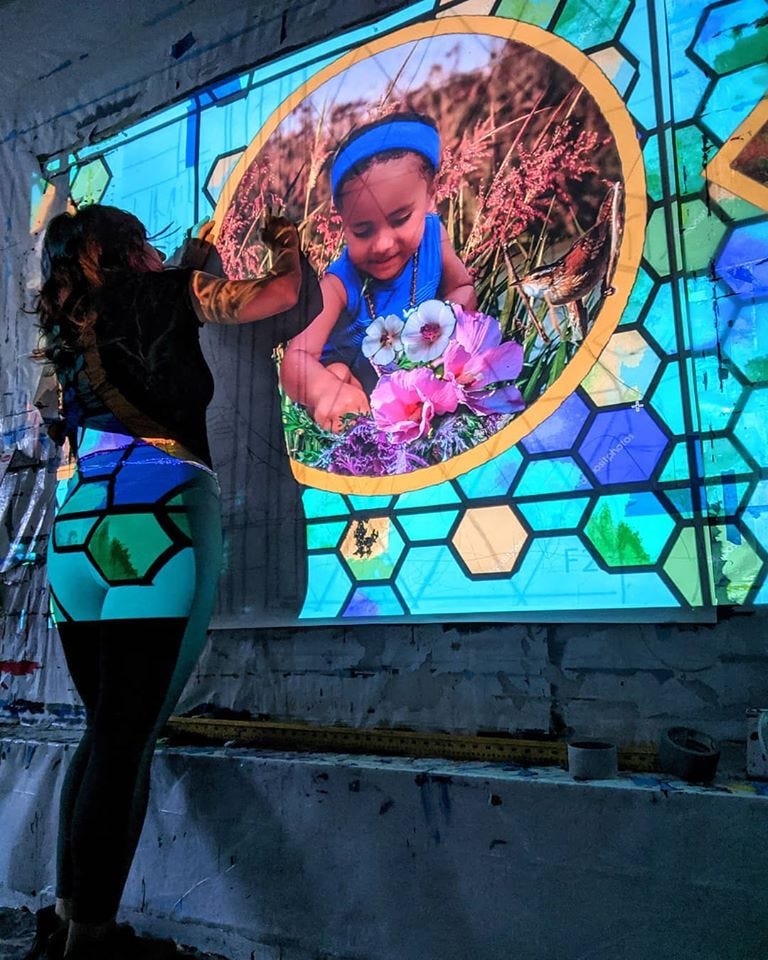 A young woman paints a wall. Projected over her is an image of a child gardening and colorful hexagons that make up the mural