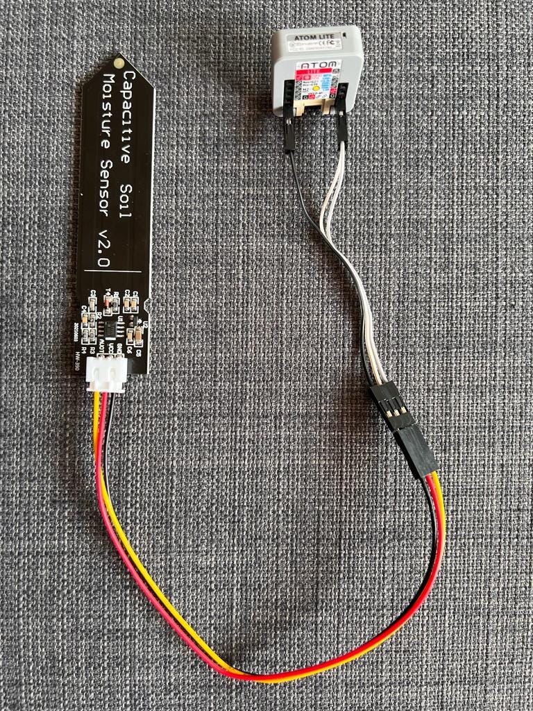 Close-up photo of the capacitive soil moisture sensor connected to the M5Atom Lite, showing the GPIO pins used