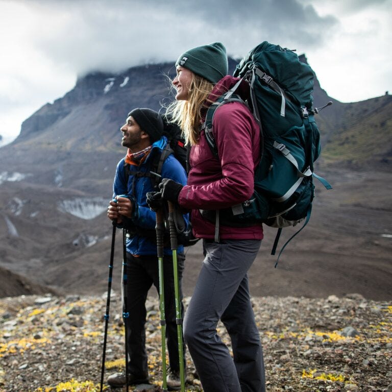 Couple backpacking on a long hike using hiking poles on a mountain.