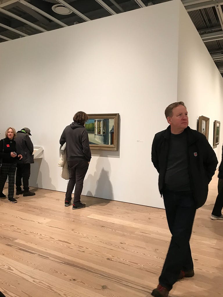 A handful of visitors at an exhibition of paintings.