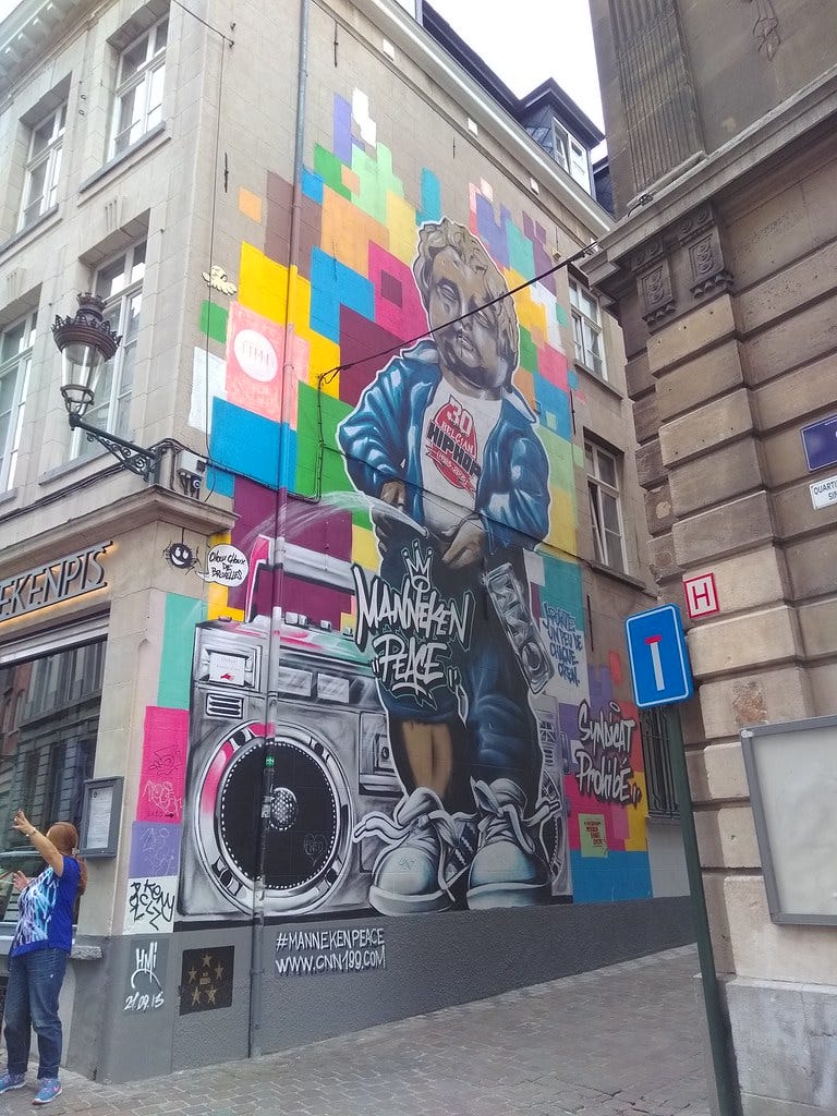 A building facade featuring a two-story depiction of Manneken Pis surrounded by colorful squares and a boombox.