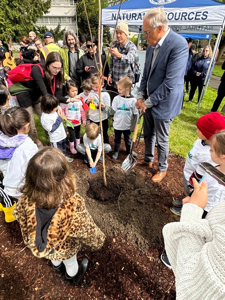 Gov. Inslee holding a shovel helping a group of kids plant a tree