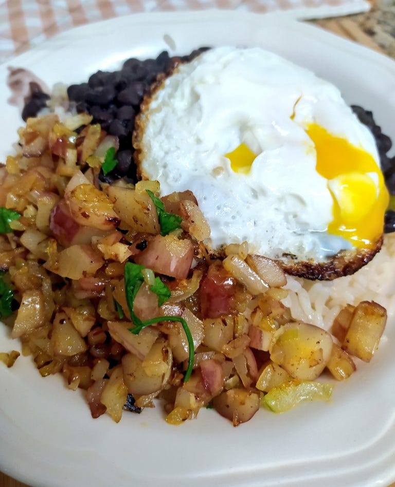 Um prato de arroz com feijão preto, farofa de pinhão e ovo frito.