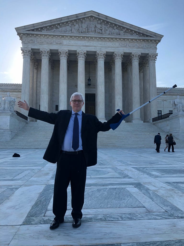 Brett McHargue, in a suit, stands in front of the Supreme Court while visiting Washington DC for the 2019 DPCA Global meeting.