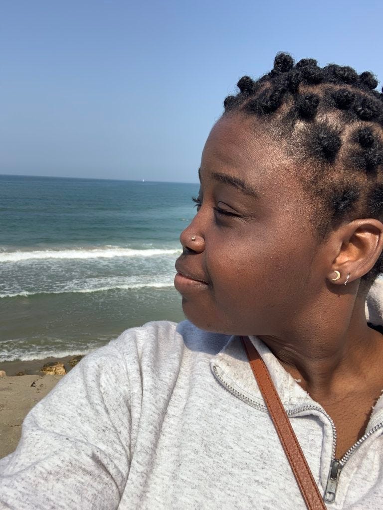 A selfie/photo from 2020 of Briayna, looking over her shoulder, by the beach in Jaffa/Tel Aviv.