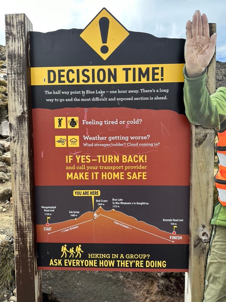 Sign reading “DECISION TIME!” and guidance about turning back if feeling tired or cold, or if the weather is getting worse. Information showing where you are on Tongariro Alpine Crossing trail (almost to peak).