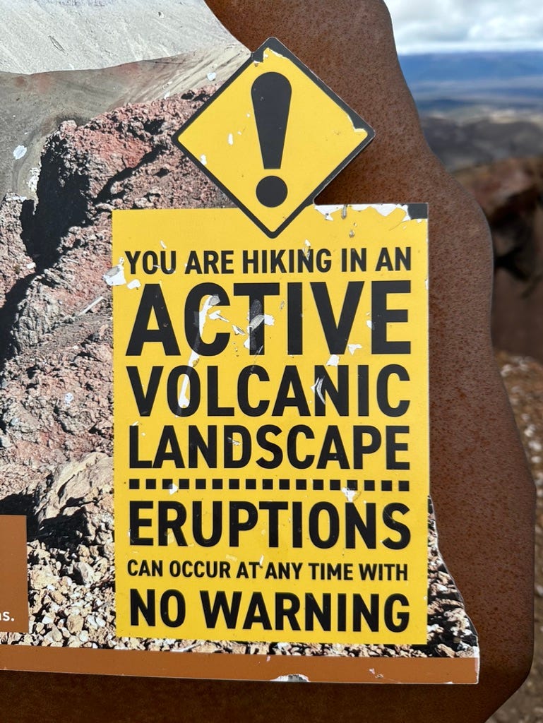 Yellow sign reading “YOU ARE HIKING IN AN ACTIVE VOLCANIC LANDSCAPE ERUPTIONS CAN OCCUR AT ANY TIME WITH NO WARNING.”