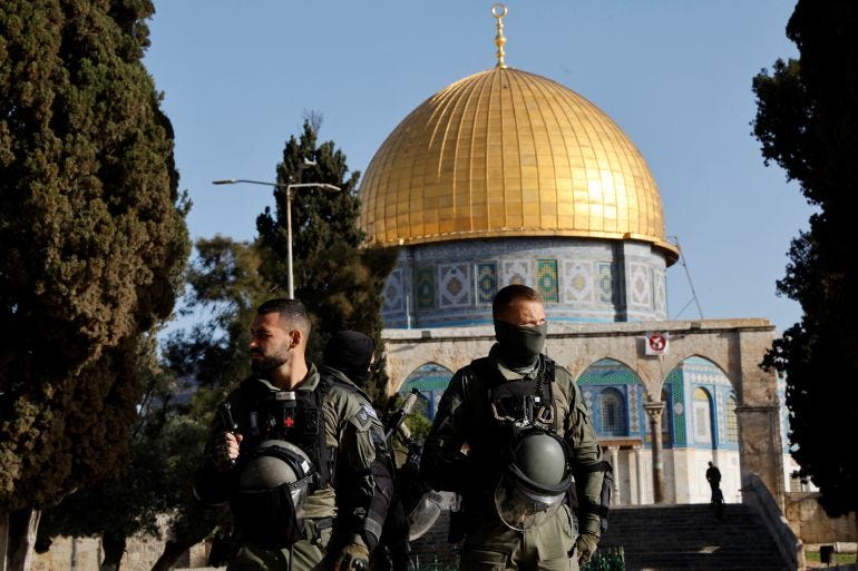 Two Israeli soldiers stand in front of a mosque with a shining golden dome