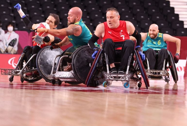 2 Danish men, and 2 Australia men playing wheelchar rugby. 2 men on the left are reaching out to grab the ball