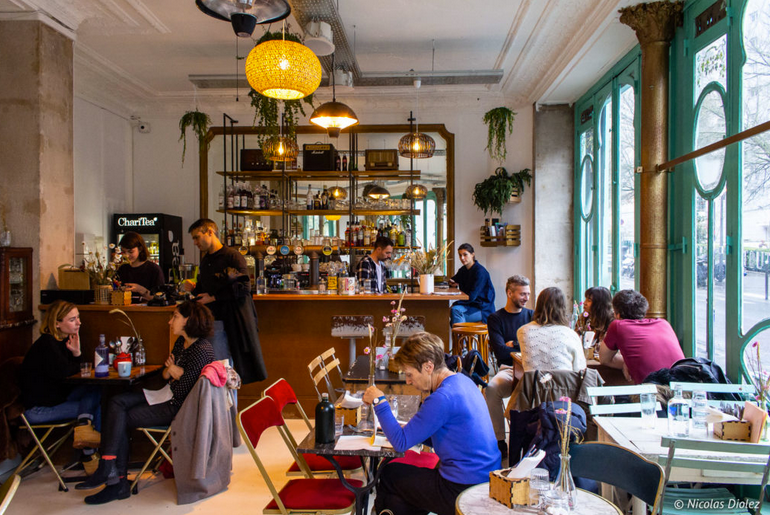 mesas cadeiras e clientes e um cafe com portas verdes e decoracao bohemia em paris