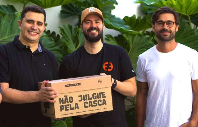 Três homens do board executivo do Mercado Diferente sorrindo para a foto, segurando uma caixa de entrega do mercado