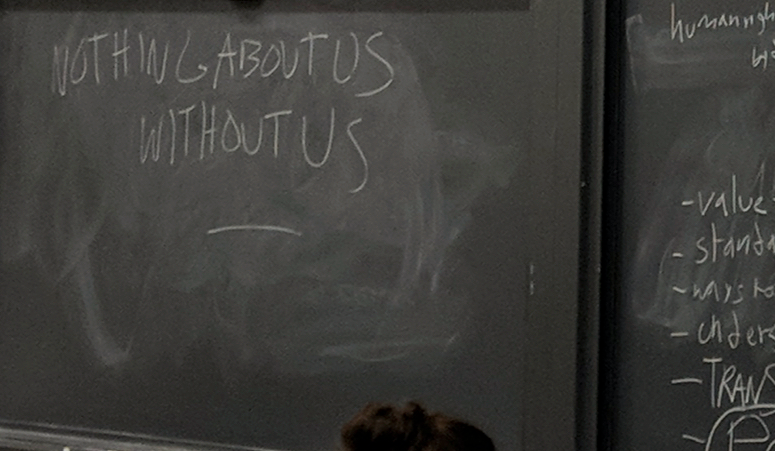 Partially erased chalkboard with the phrase “Nothing about us without us”