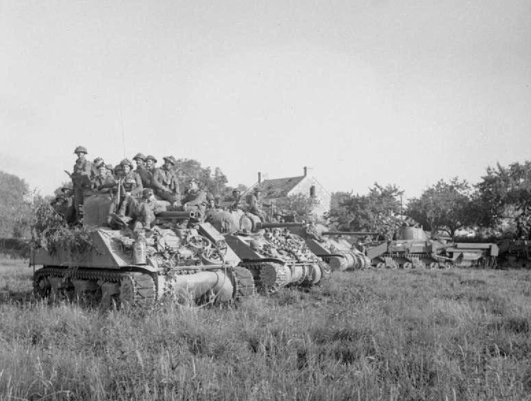 A fleet of tanks and soldiers sit in a field.