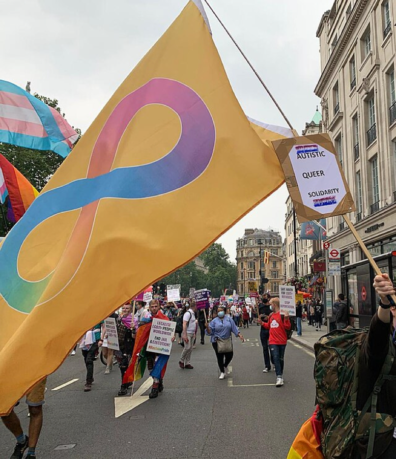 Autistic Pride Flag at Pride. Gold is used by autistic advocates as the chemical symbol for gold is Au. The infinity symbol represents the broad and varied spectrum of experiences within neurodiversity, the rainbow represents the pride movement.
