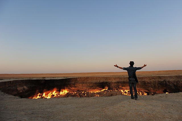 A man standing with arms outstretched in front of the Darvaza gas crater