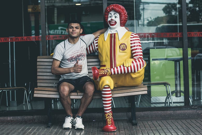 A man sitting on a bench beside a statue of Ronald McDonald