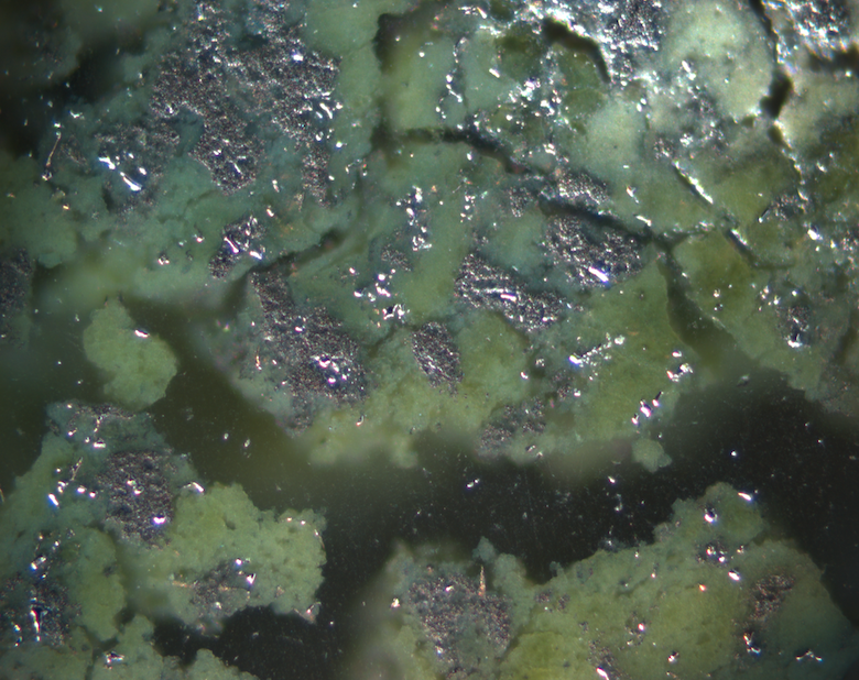 Close-up shows shiny metal patches with areas of green corrosion and open holes.
