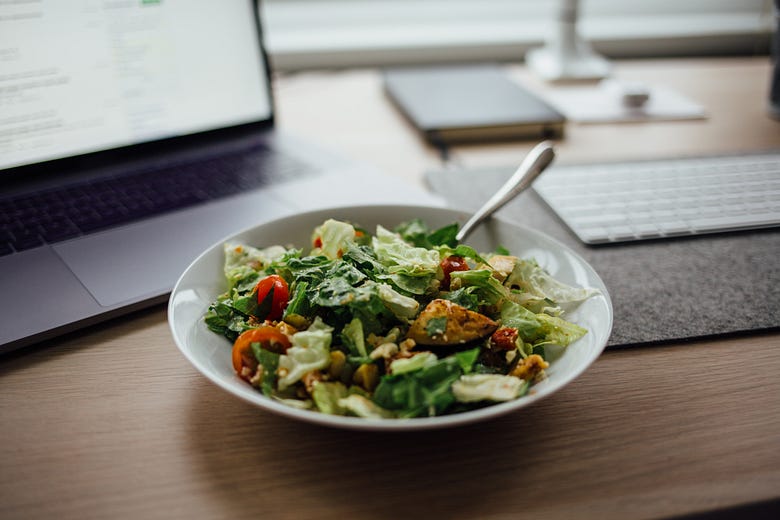 A bowl of Caesar salad in front of a laptop.