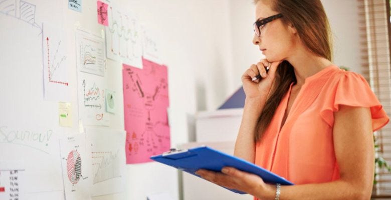 A female designer looking at pieces of paper pinned on a whiteboard.