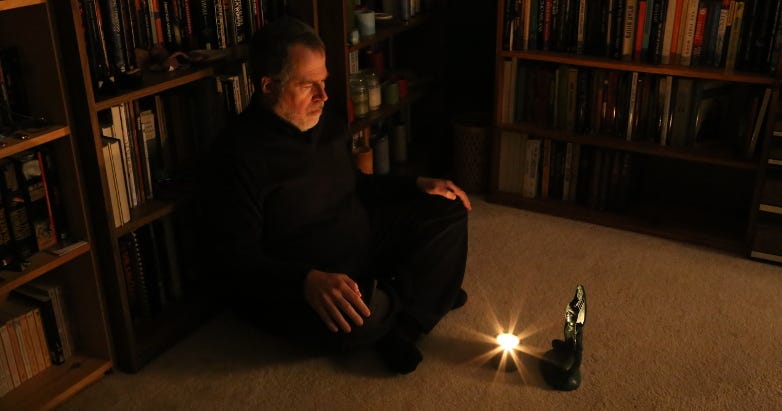 A person sitting in front of a candle and a statue.