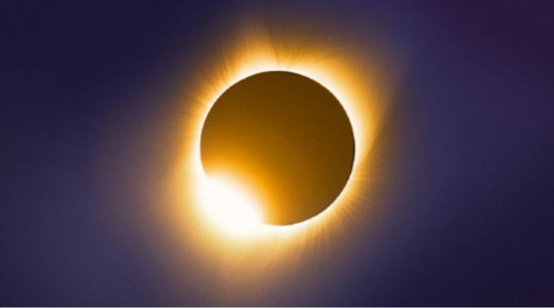 A dark moon covers the sun creating a halo effect. The bright edges of the sun are still visible under the moon.