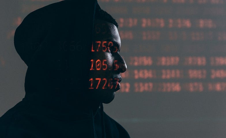 A young black man in a hoodie sitting in the dark with numbers flashing across his face and in the background.