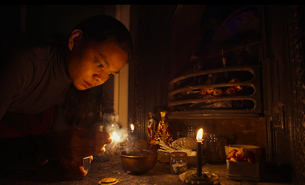 Film still from Nocebo shows Filipino maid Diana before relics, talismans, a candle, and other shamanistic tools.