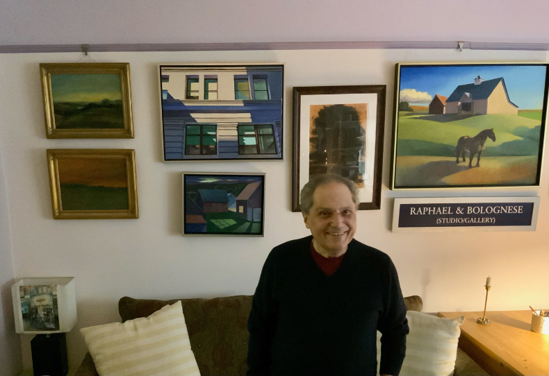 Don Bolognese standing in front of some of his artwork on the wall.