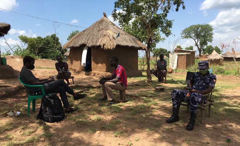 Five people sit in chairs outside a hut under a blue sky.