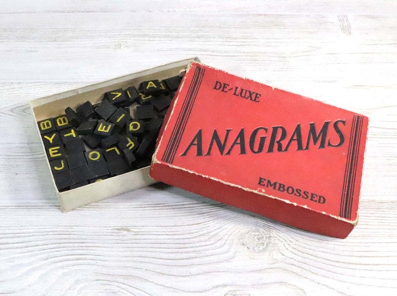 an antique board game box labeled “de-luxe anagrams”. the box is open showing scrabble-like tiles inside.