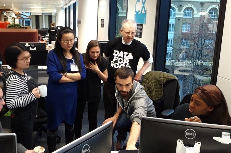 Group of adults around a computer monitor in an office, one is pointing directly at something on screen