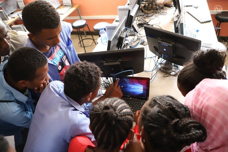 A group of people gathered around a computer in what looks like a school
