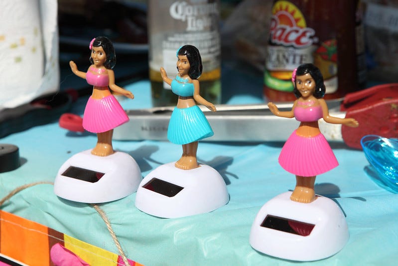 Three solar hula dancer figurines on a shelf in the sun