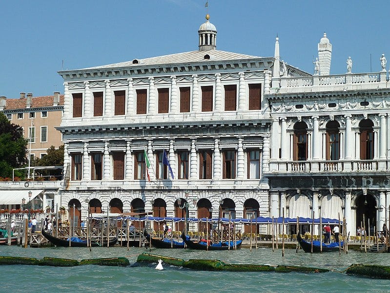 Zecca in Venice. The building is painted in a bright white paint and covered in windows.