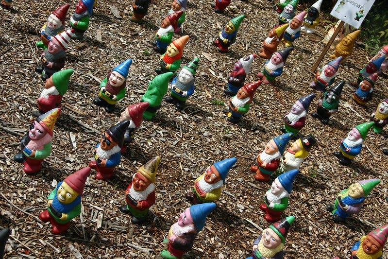 A disconcerting number of gnomes on a dirt field.