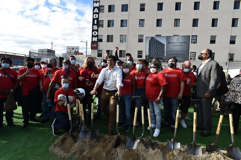 A group of people stand in front of a pile of dirt with shovels in hand.