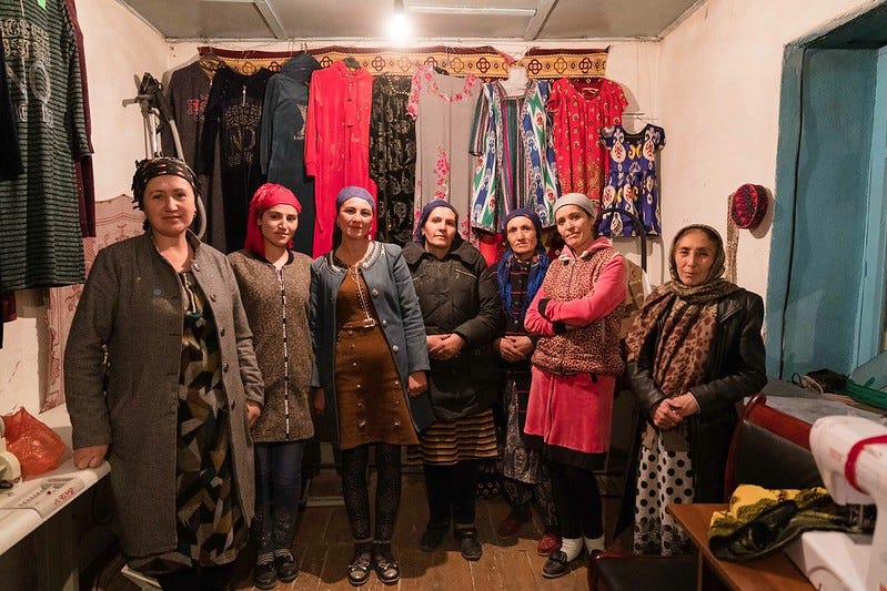 Roziyamo (in pink) and her team of seamstresses stand in front of clothing they have sewn.