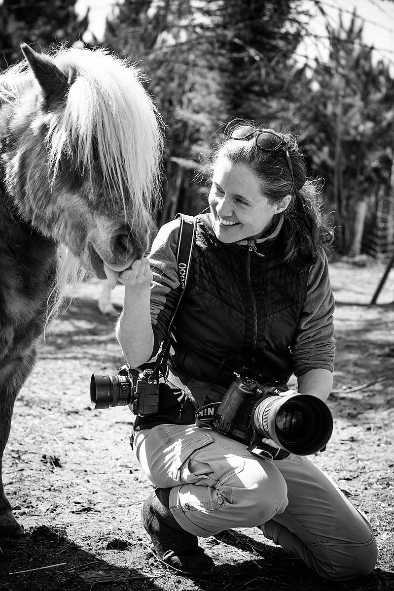 Animal photojournalist Jo-Anne McArthur smiles as Bronco the pony sniffs her hand in search of treats. SAFE — Sanctuaire pour animaux de ferme de l’Estrie, Potton, Quebec, Canada, 2021. Victoria de Martigny / We Animals Media