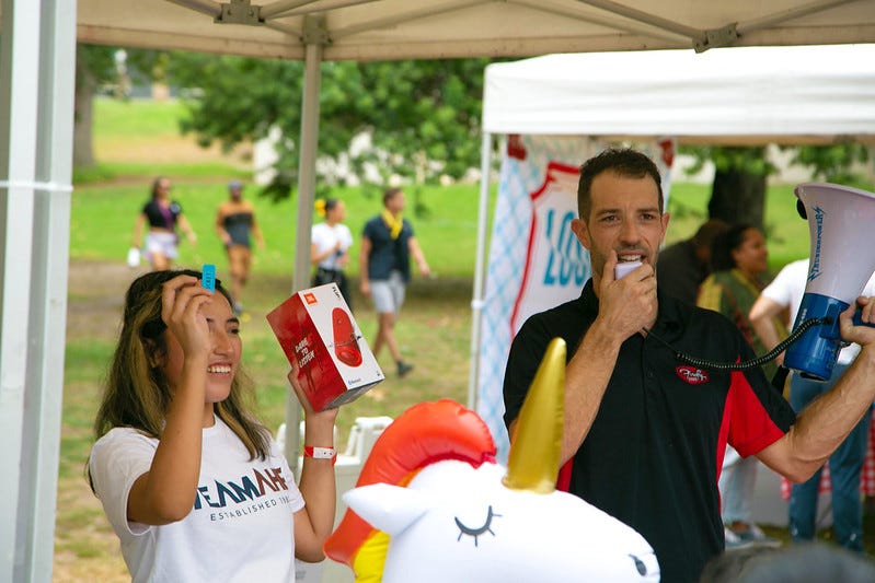A girl holds up a raffle ticket and speaker prize while a winner is being announced at a park.
