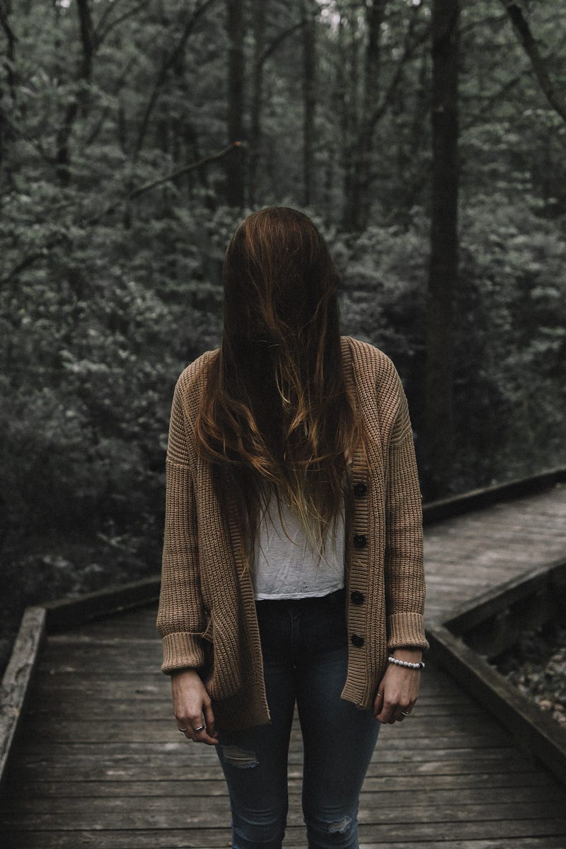 Lady with cardigan with her head bent and hair astray.