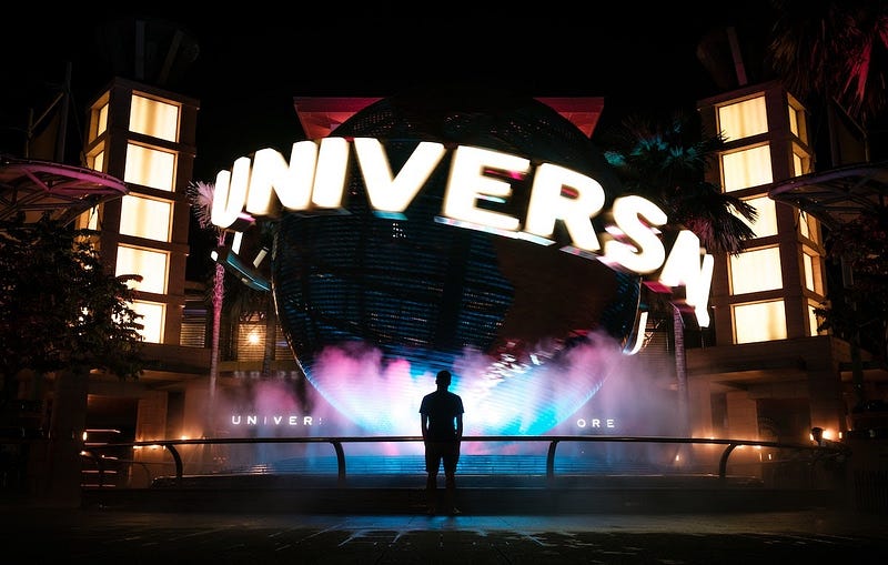 A person stands in front of hte entrance to Universal Studios at the huge globe. It is night time and the entrance is lit up.