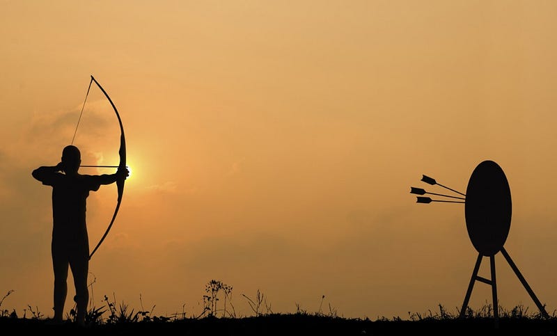 Silhouette archery shoots a bow at the target in sunset sky and cloud.